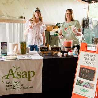 Interns Kelsie Rothwell and Holly Kolarova offer fruit slushies at River Arts District Farmers Market