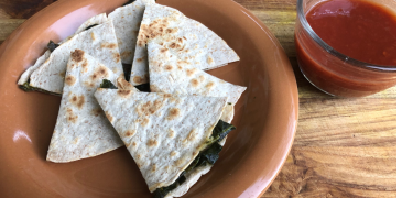 quesadilla with local greens on orange plate with red sauce on the side