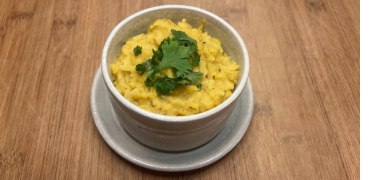 yellow kitchari in a white bowl with cilantro on top