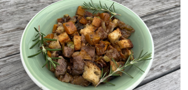 butternut, apple, and brussels sprouts stuffing with three pieces of rosemary garnish in a sage green bowl on a wood background