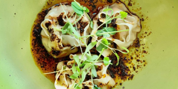 dumplings on a lime colored plate with chili oil and microgreens on top