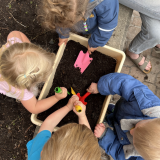 an overhead shot of four white children digging in soil with trowelswit