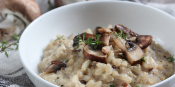 white bowl on a striped kitchen towel filled with mushroom risotto