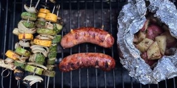 Summer squash skewers, brats, and potatoes on a grill