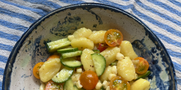 gnocchi summer salad with cucumbers, cherry tomatoes, and corn in a blue and white bowl